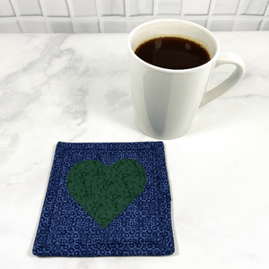 Mug rugs are also known as drink coasters. They are made from 100% cotton fabric, are insulated and washable too. These are great accessories for your home office desk or for your coffee bar area. This particular one is made with a blue background with a dark green appliqued heart in the center.