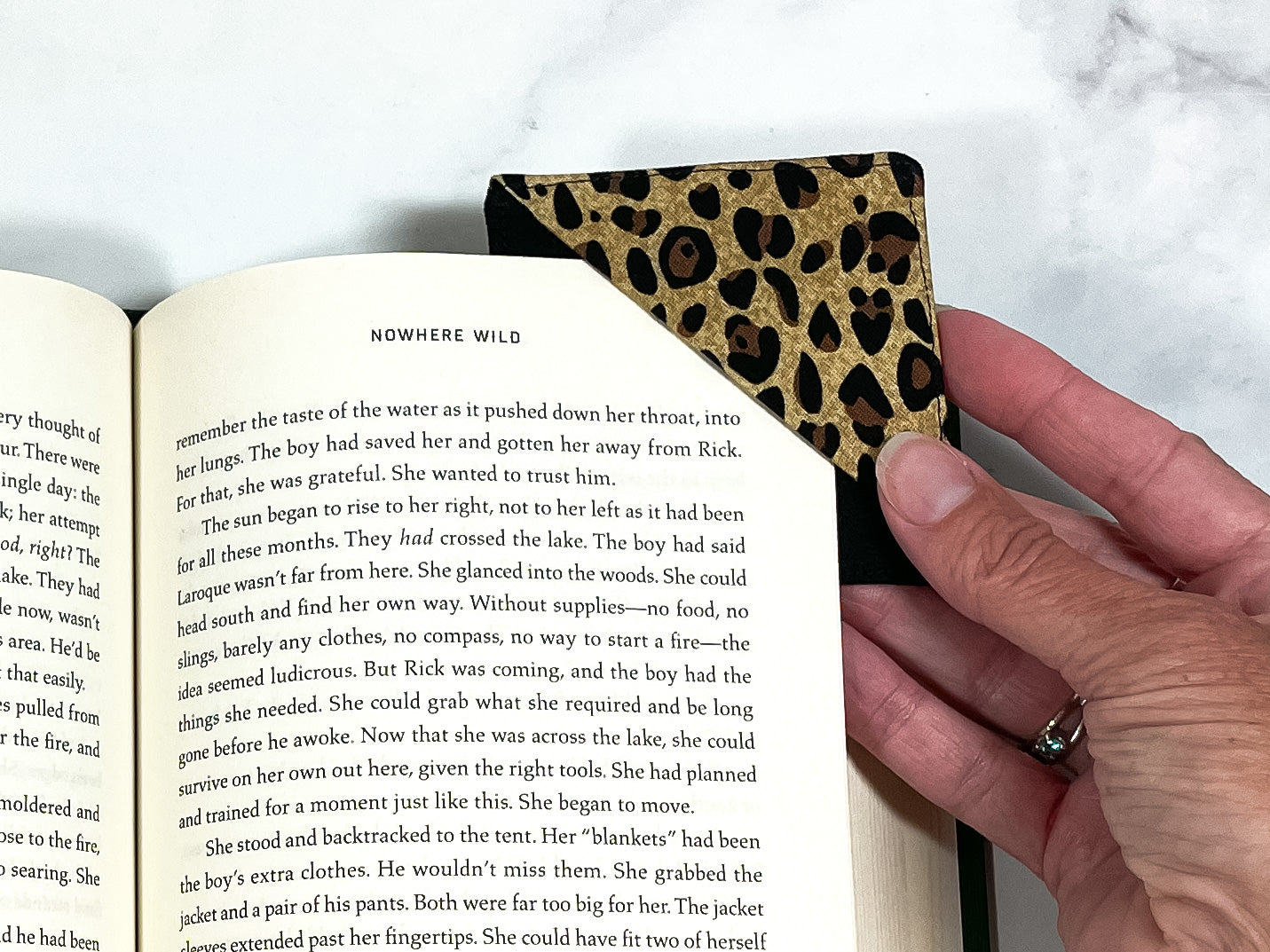 A handmade corner bookmark made from a fun leopard print themed cotton fabric in shades of brown, gold and black.  The page marker is square and is being shown sliding over the corner of a page in a book.