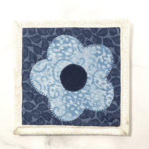 Mug rugs are also known as drink coasters. They are made from 100% cotton fabric, are insulated and washable too. These are great accessories for your home office desk or for your coffee bar area. This particular one is made with blue and white fabrics with a flower appliqued in the center.