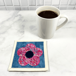 Mug rugs are also known as drink coasters. They are made from 100% cotton fabric, are insulated and washable too. These are great accessories for your home office desk or for your coffee bar area. This particular one is made pink and blue fabrics with a flower appliqued in the center.