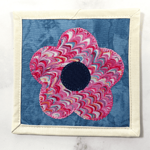 Mug rugs are also known as drink coasters. They are made from 100% cotton fabric, are insulated and washable too. These are great accessories for your home office desk or for your coffee bar area. This particular one is made pink and blue fabrics with a flower appliqued in the center.
