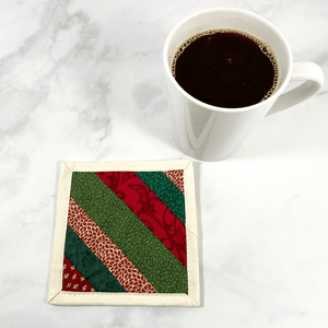 Mug rugs are also known as drink coasters. They are made from 100% cotton fabric, are insulated and washable too. These are great accessories for your home office desk or for your coffee bar area. This particular one is made with green and red patterned fabrics, in a strip pieced design.