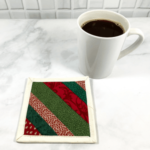 Mug rugs are also known as drink coasters. They are made from 100% cotton fabric, are insulated and washable too. These are great accessories for your home office desk or for your coffee bar area. This particular one is made with green and red patterned fabrics, in a strip pieced design.