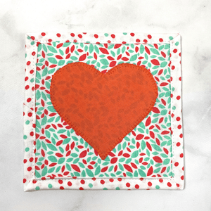 Mug rugs are also known as drink coasters. They are made from 100% cotton fabric, are insulated and washable too. These are great accessories for your home office desk or for your coffee bar area. This particular one is made with a fun coral and aqua speckled fabric background and a solid coral heart appliqued in the center.