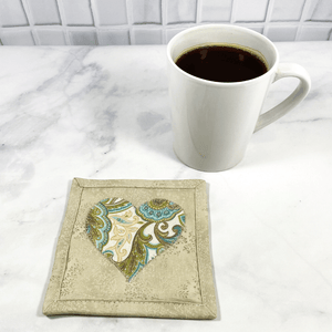Mug rugs are also known as drink coasters. They are made from 100% cotton fabric, are insulated and washable too. These are great accessories for your home office desk or for your coffee bar area. This particular one is made with a beige background and a gorgeous beige and aqua paisley fabric heart appliqued in the center.