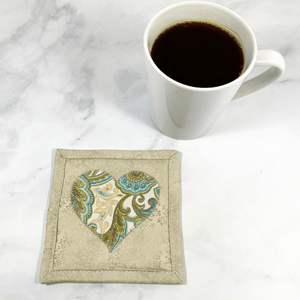 Mug rugs are also known as drink coasters. They are made from 100% cotton fabric, are insulated and washable too. These are great accessories for your home office desk or for your coffee bar area. This particular one is made with a beige background and a gorgeous beige and aqua paisley fabric heart appliqued in the center.