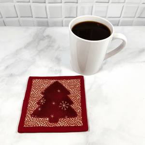 This is a mug rug aka drink coaster that has a gorgeous burgundy and cream Christmas tree applique pattern on the front.  These mug rugs make a great gift for the coffee lover in your life.  It brightens up any table or desk.