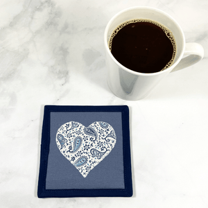 Mug rugs are also known as drink coasters. They are made from 100% cotton fabric, are insulated and washable too. These are great accessories for your home office desk or for your coffee bar area. This particular one is made with blue, gray and white fabrics with a paisley designed heart appliqued in the center.