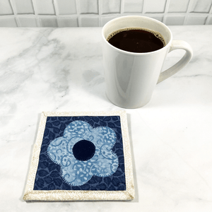 Mug rugs are also known as drink coasters. They are made from 100% cotton fabric, are insulated and washable too. These are great accessories for your home office desk or for your coffee bar area. This particular one is made with blue and white fabrics with a flower appliqued in the center.