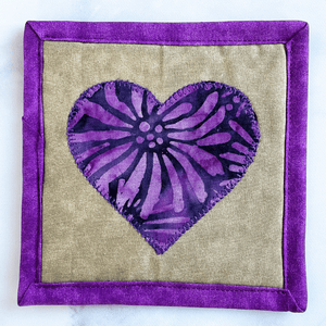 This is a purple batik fabric heart mug rug. Mug rugs are also known as drink coasters.  They are made from 100% cotton fabric, are insulated and washable too.  These are great accessories for your home office desk or for your coffee bar area, adding a splash of color and uniqueness.